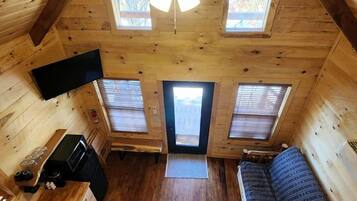 A cozy cabin with a loft bedroom, a kitchenette, and a large window.