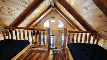 Une chambre située sous les combles, avec des poutres apparentes, un plafond en pente et une fenêtre centrale.