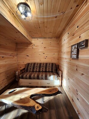 Interior de una cabaña de madera con sofá, una mesa de centro de madera única y una lámpara de techo.