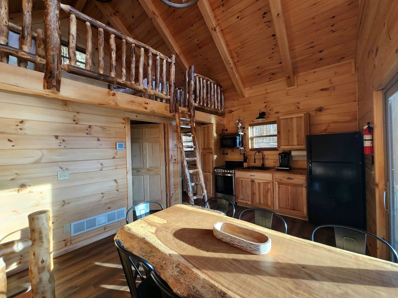 A wooden cabin interior with a dining area, kitchen, and a loft bedroom.
