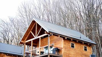 A log cabin with a stone foundation, a balcony, and a metal roof.