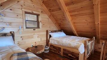 Ein gemütliches Schlafzimmer im Dachgeschoss mit zwei hölzernen Betten, einem kleinen Tisch und einem Deckenventilator.