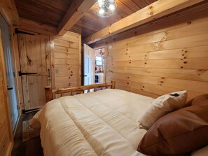 Dormitorio de cabaña de madera con una cama, almohadas y techo de madera.