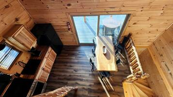 A wooden interior with a dining table, kitchen area, and a large window.