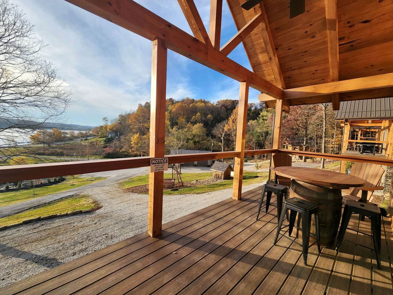 Una terraza de madera con una mesa y sillas, con vista a un área de grava y una carretera.