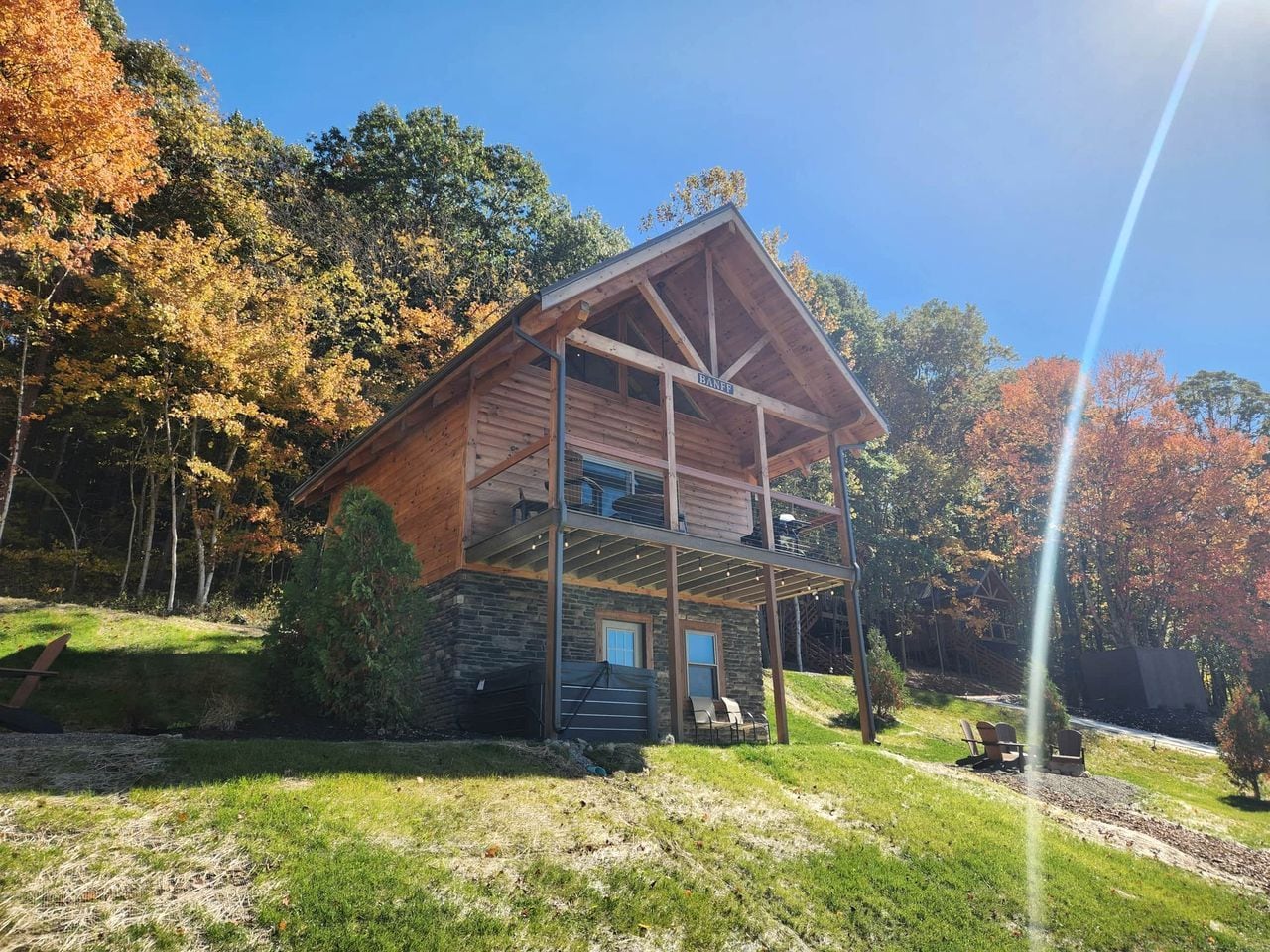 Eine zweistöckige Blockhütte mit Veranda, umgeben von Bäumen und einem klaren Himmel.