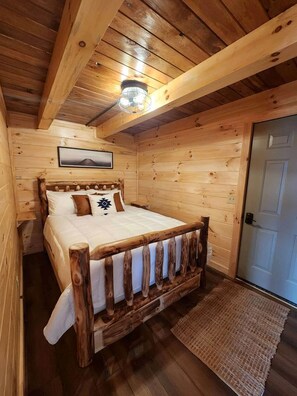 Ein Schlafzimmer einer Holzhütte mit Bett, Deckenleuchte und Tür.