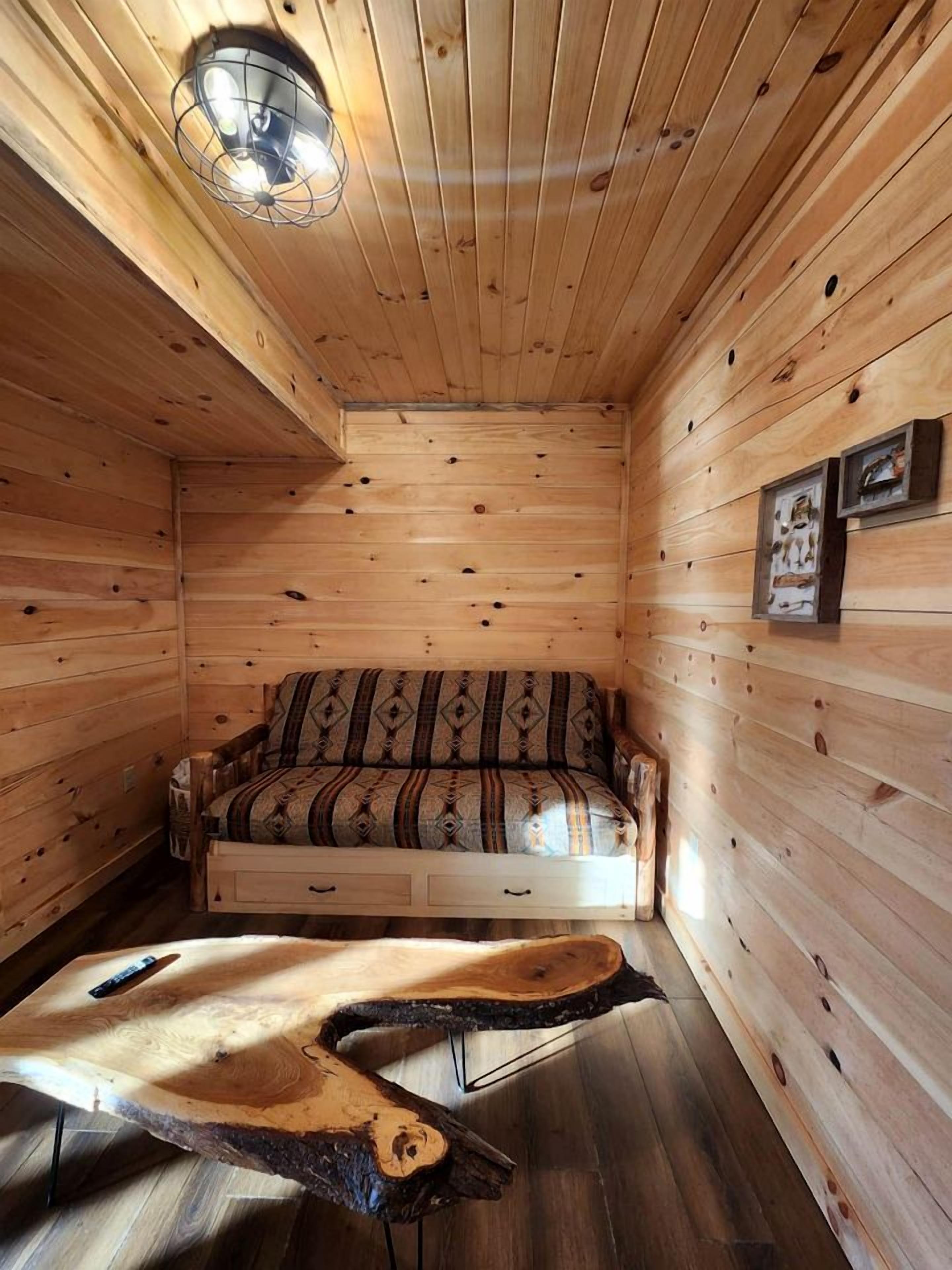 Ein Holzblockhaus-Innenraum mit einer Couch, einem einzigartigen Couchtisch aus Holz und einer Deckenleuchte.
