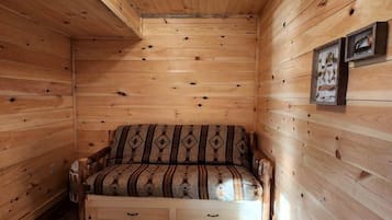 Ein Holzblockhaus-Innenraum mit einer Couch, einem einzigartigen Couchtisch aus Holz und einer Deckenleuchte.