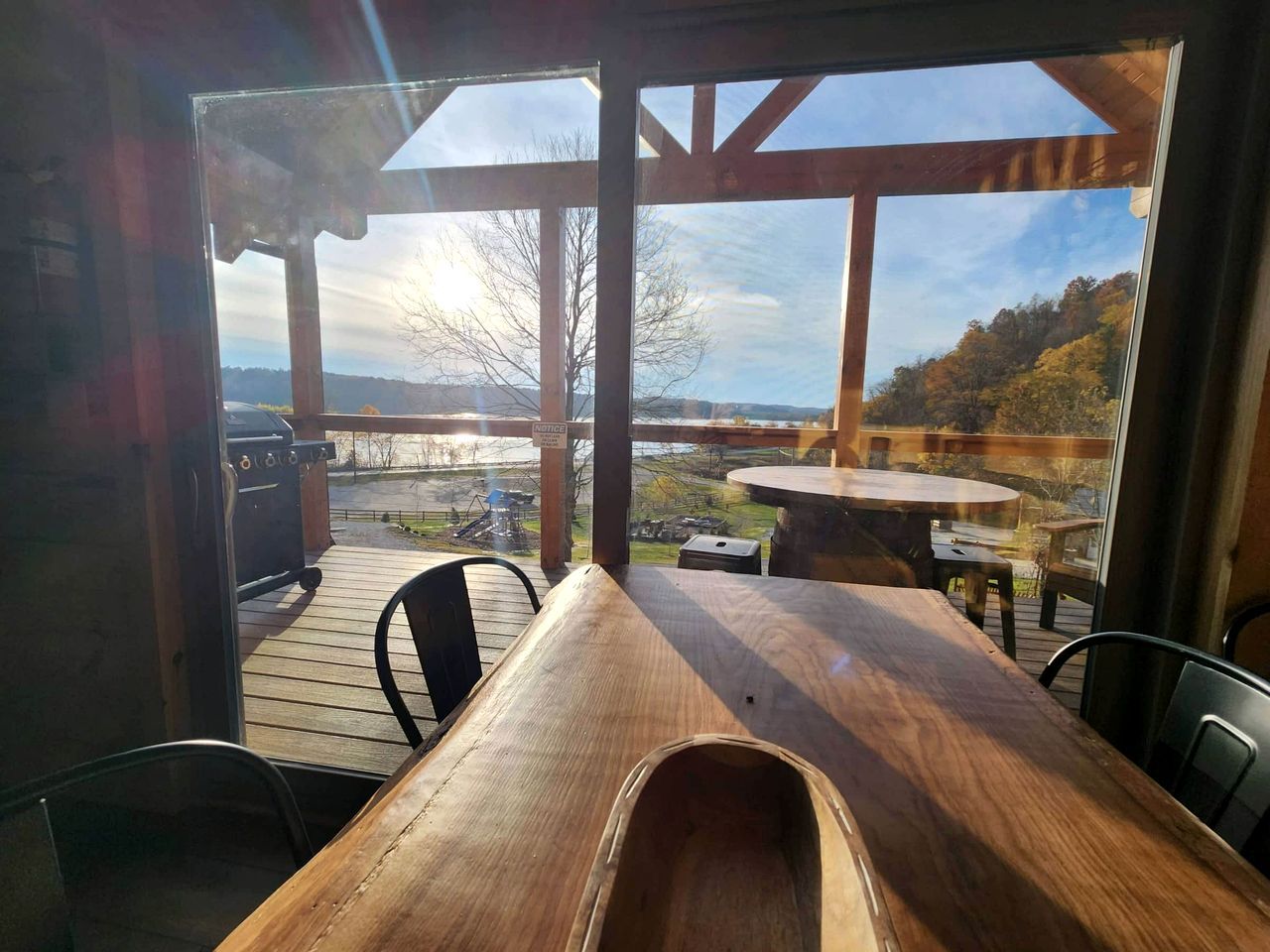 Una terraza de madera al aire libre con una mesa y sillas, con vistas a un paisaje pintoresco con árboles y una lejana perspectiva.