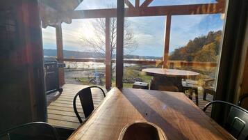 Una terraza de madera al aire libre con una mesa y sillas, con vistas a un paisaje pintoresco con árboles y una lejana perspectiva.