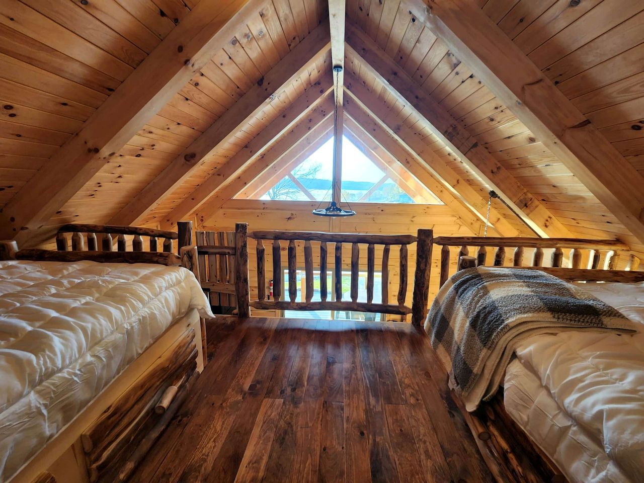 Dormitorio tipo loft con dos camas, vigas de madera, tragaluces y vistas al exterior.