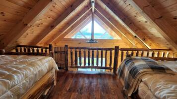 Dormitorio tipo loft con dos camas, vigas de madera, tragaluces y vistas al exterior.