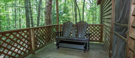 A wooden deck with a bench and a lattice railing, surrounded by trees.