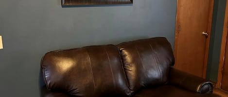 A brown leather sofa against a dark wall with a framed picture above it.