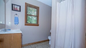 Ein Badezimmer mit einem Holzkosmetikschrank, einem Fenster mit Jalousien, einer Toilette und einer Duschkabine.