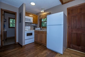 A kitchen with wooden cabinets, a white refrigerator, a stove, and a window with blinds. - North Carolina Pet-Friendly Cabin Rental for Romantic Getaways to the Mountains (Spruce Pine)