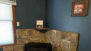 Una habitación con pared de piedra, chimenea y ventana con persianas.