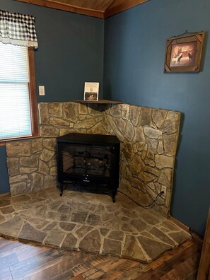 Una habitación con pared de piedra, chimenea y ventana con persianas.