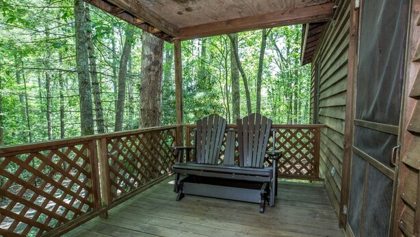 Une terrasse en bois, dotée d’un banc et d’une balustrade en treillis, entourée d’arbres.
