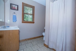 Ein Badezimmer mit einem Holzkosmetikschrank, einem Fenster mit Jalousien, einer Toilette und einer Duschkabine.