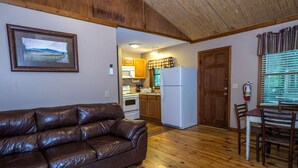 Ein gemütlicher Wohnbereich mit einer braunen Ledersofa, Holzböden, einer Küche mit Holzschränken, einem weißen Kühlschrank und einem Esstisch mit Stühlen.