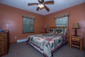 A bedroom with a bed, two windows with blinds, a ceiling fan, a nightstand with a lamp, and a dresser. - North Carolina Pet-Friendly Cabin Rental for Romantic Getaways to the Mountains (Spruce Pine)