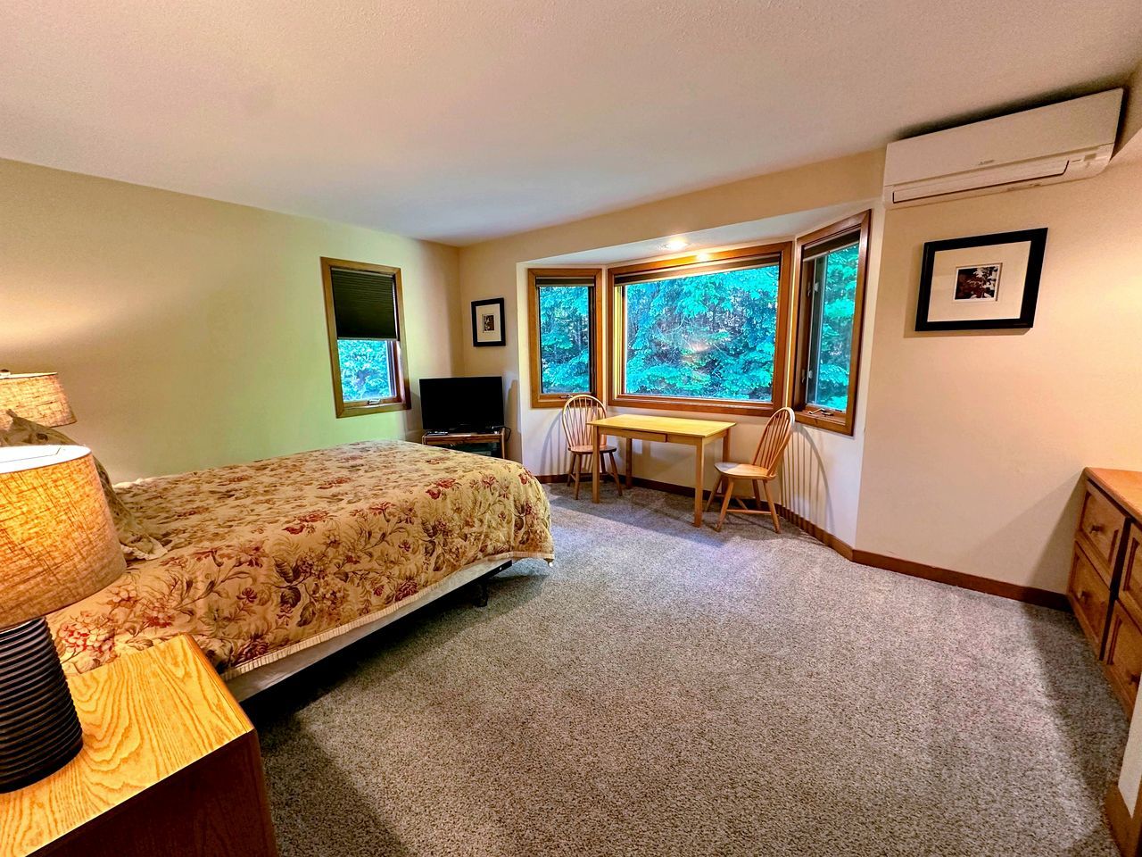 Une chambre à coucher avec un lit, un bureau, une chaise et une fenêtre donnant sur des arbres.