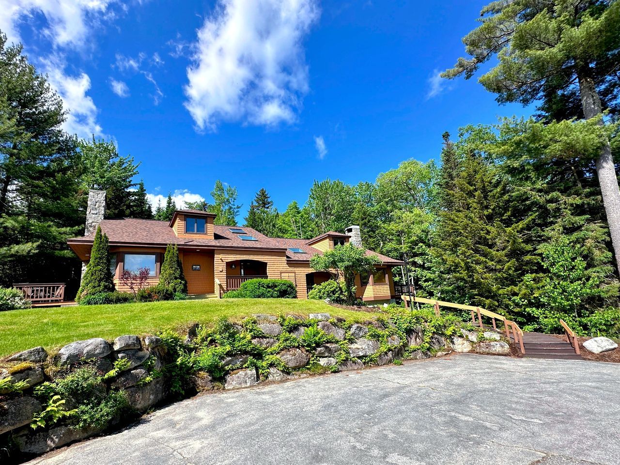 A two-story house with a stone chimney, a stone retaining wall, and a wooden deck.