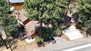 An aerial view of a residential area with a house, a car parked in front, and surrounding trees. - Adventure Awaits: Big Bear Lake Mountain Cabin with Game Room + Hot Tub (Big Bear Lake)