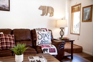 A cozy living room with a brown leather sofa, a coffee table with a plant and glasses, a bear wall decoration, a lamp, and a framed picture on the wall. - Adventure Awaits: Big Bear Lake Mountain Cabin with Game Room + Hot Tub (Big Bear Lake)