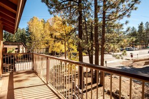 A wooden balcony with a metal railing overlooking a street with autumn trees and a stop sign. - Adventure Awaits: Big Bear Lake Mountain Cabin with Game Room + Hot Tub (Big Bear Lake)