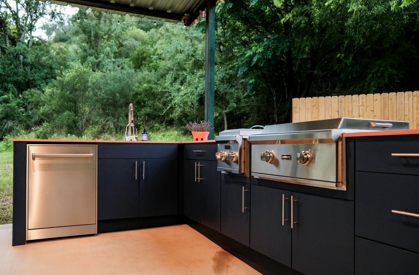 Una cocina moderna al aire libre con horno empotrado, un lavaplatos y una encimera.