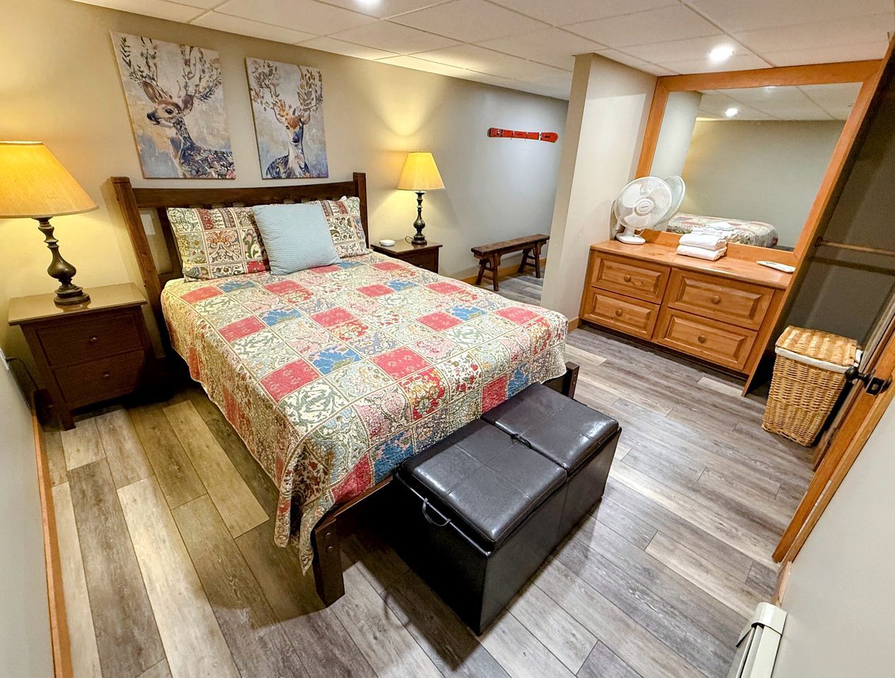 Een slaapkamer met een bed, nachtlampen, een bankje, een dressoir en een spiegel.