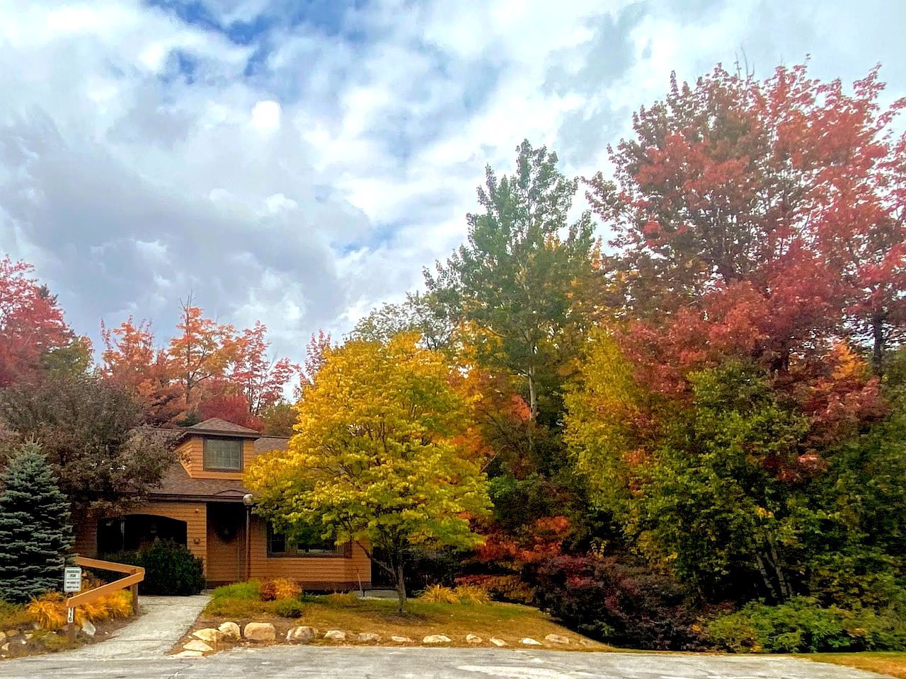 A two-story house with a covered driveway and a front yard with various trees.