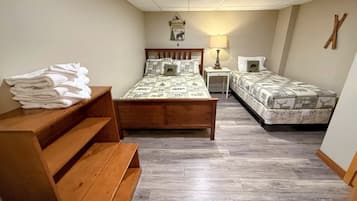 A room with two beds, a wooden bench, a lamp, and a wall-mounted decoration.
