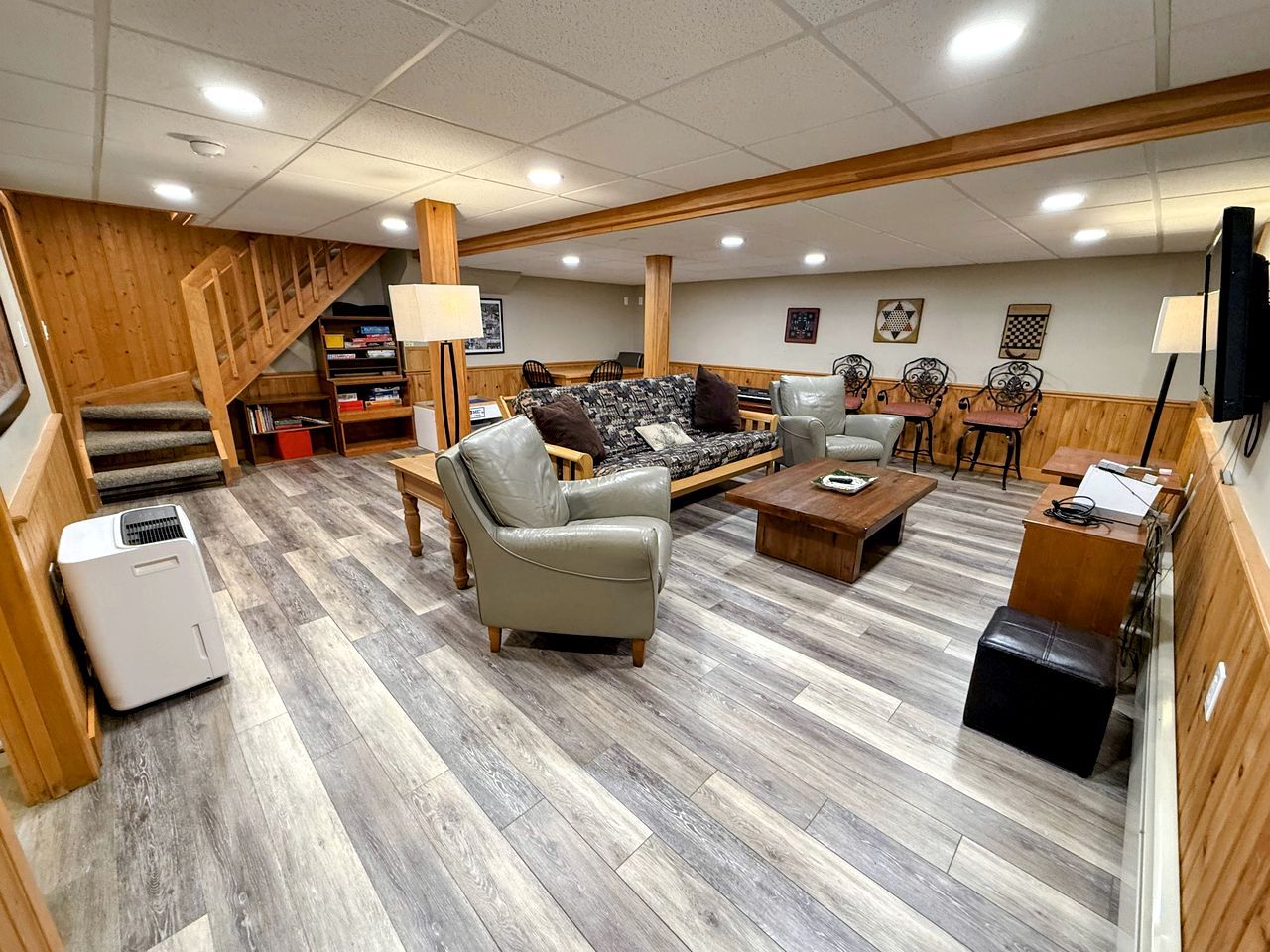 A spacious living area with a sofa, armchairs, a coffee table, and a fireplace. A staircase with wooden railings leads to an upper level.