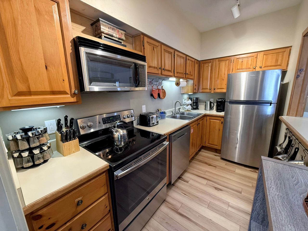 A modern kitchen with wooden cabinets, stainless steel appliances, and a wooden floor.