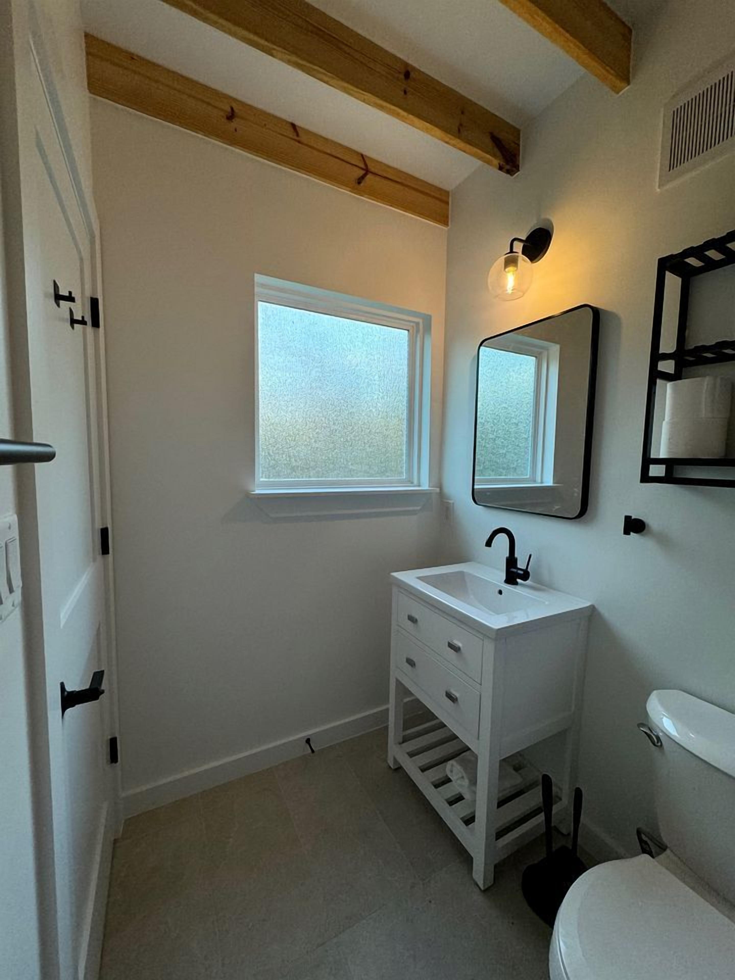Un baño con lavamanos blanco, un espejo, una ventana y un inodoro.