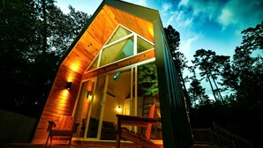 Una cabaña moderna de madera con techo inclinado, amplios ventanales de vidrio y una terraza de madera.