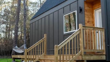 A cabin with a wooden staircase leading to a deck, surrounded by trees.
