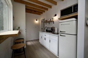 Une cuisine de taille réduite avec des meubles blancs, un réfrigérateur, un four à micro-ondes et un plafond avec une poutre en bois.
