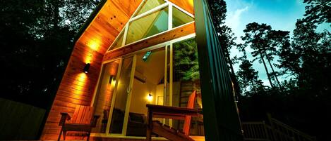 Una cabaña moderna de madera con techo inclinado, amplios ventanales de vidrio y una terraza de madera.