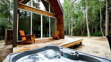 En træhytte med jacuzzi, terrassedøre og skov i baggrunden.