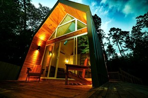 A modern wooden cabin with a sloped roof, large glass windows, and a wooden deck. - Luxury Cabin with Private Hot Tub - Cueta, Montgomery, TX (Montgomery)