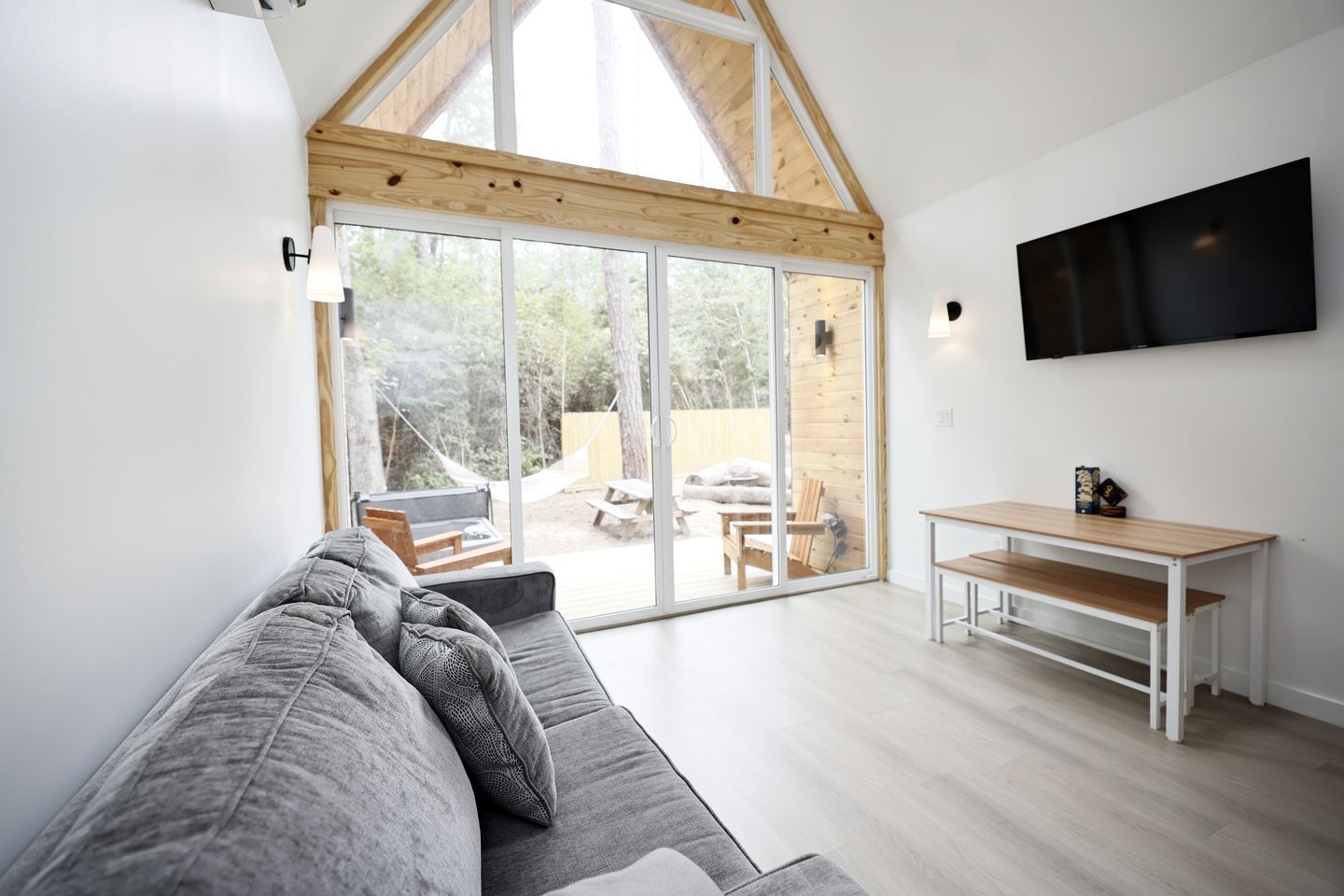 A modern interior with a grey sofa, a wooden dining table, and a TV mounted on the wall.