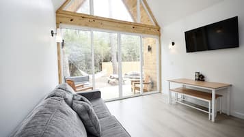 A modern interior with a grey sofa, a wooden dining table, and a TV mounted on the wall.