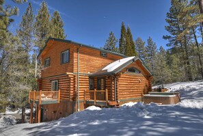 Eine Blockhütte mit Veranda, umgeben von Schnee und Kiefern.