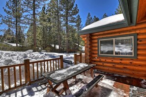 A wooden cabin with a deck and a window, surrounded by snow and trees. - Escape to Adventure: Mountain Cabin Holidays in Big Bear Lake (Big Bear Lake)