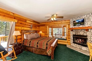 Ein Schlafzimmer in einer Blockhütte mit einem Bett, einem Kamin, einem Fernseher und einem Fenster mit Rollläden.